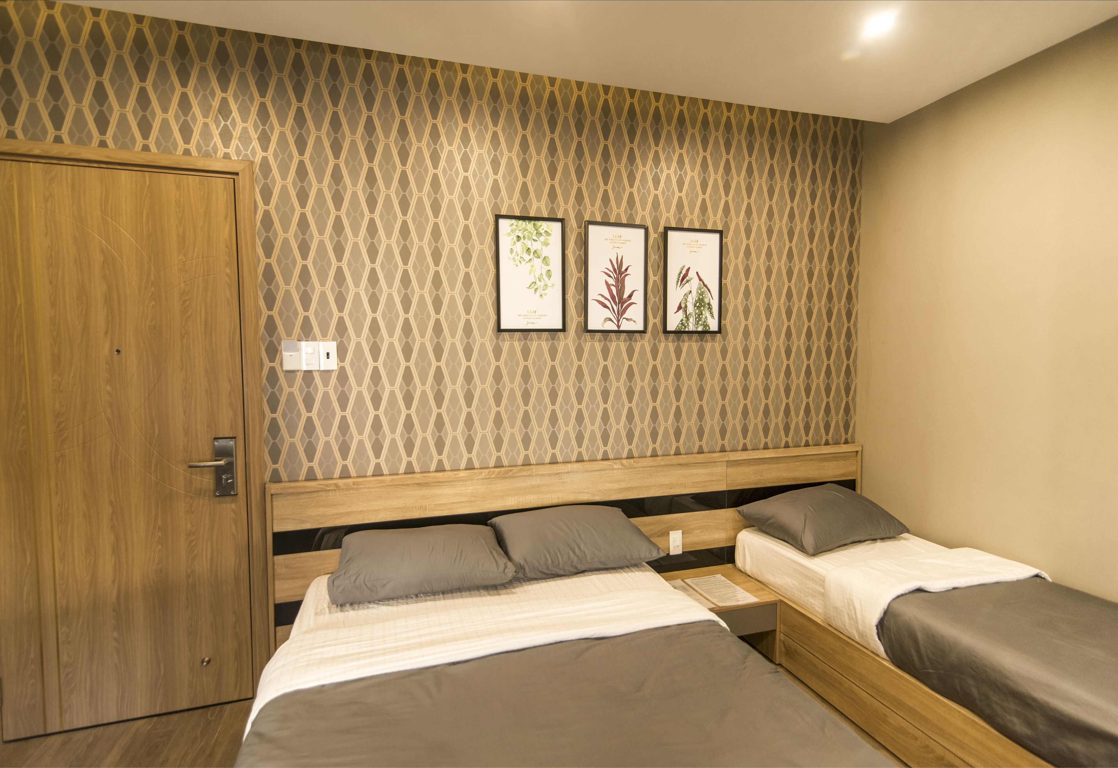 A bedroom with a wooden wardrobe, a bed with grey bedding, and three framed botanical prints on the wall.