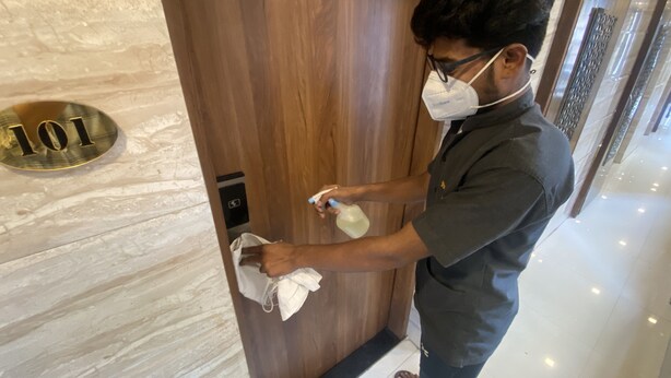 A person cleaning a wooden elevator door with a sign indicating room number 101. - Hotel Apsara Near JJ Hospital (Mumbai)