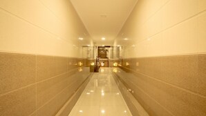A corridor with reflective tiled floors and walls, leading to a reception area with a counter and lighting fixtures. - Hotel Apsara Near JJ Hospital (Mumbai)