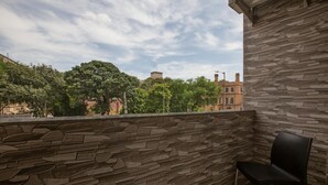 A balcony with a stone wall, a black chair, and a view of trees and buildings. - Hotel Apsara Near JJ Hospital (Mumbai)