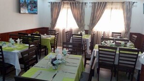 A dining area with multiple tables set for meals, air conditioning units, and curtains on the windows. - Hotel Samaki Plage (Kribi)