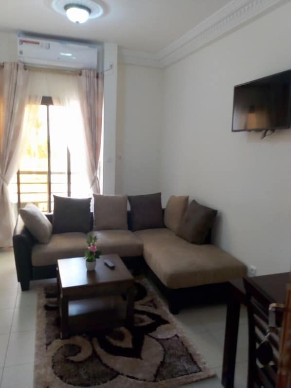 A living room with a sofa, a coffee table, and a TV mounted on the wall. - Hotel Samaki Plage (Kribi)