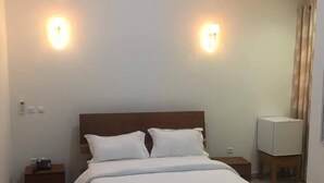 A hotel room with a large bed, two bedside tables, a flat-screen TV, and a ceiling light fixture. - Hotel Samaki Plage (Kribi)