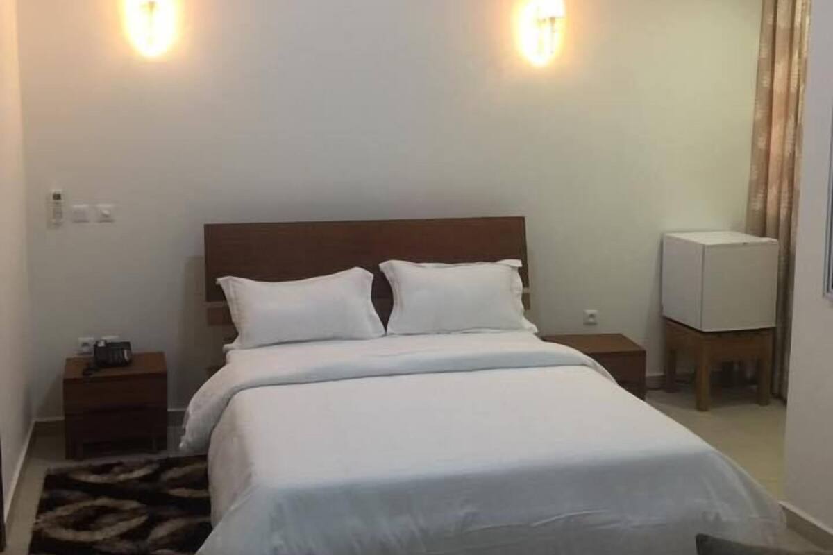 A hotel room with a large bed, two bedside tables, a flat-screen TV, and a ceiling light fixture.