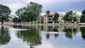 A tranquil lakeside view with a multi-story building featuring balconies and a tiled roof.