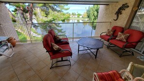 A covered patio with red chairs and a table, overlooking a lake and greenery.