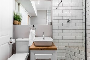 A modern bathroom with a white sink on a wooden countertop, a toilet, and a shower area with white tiles.