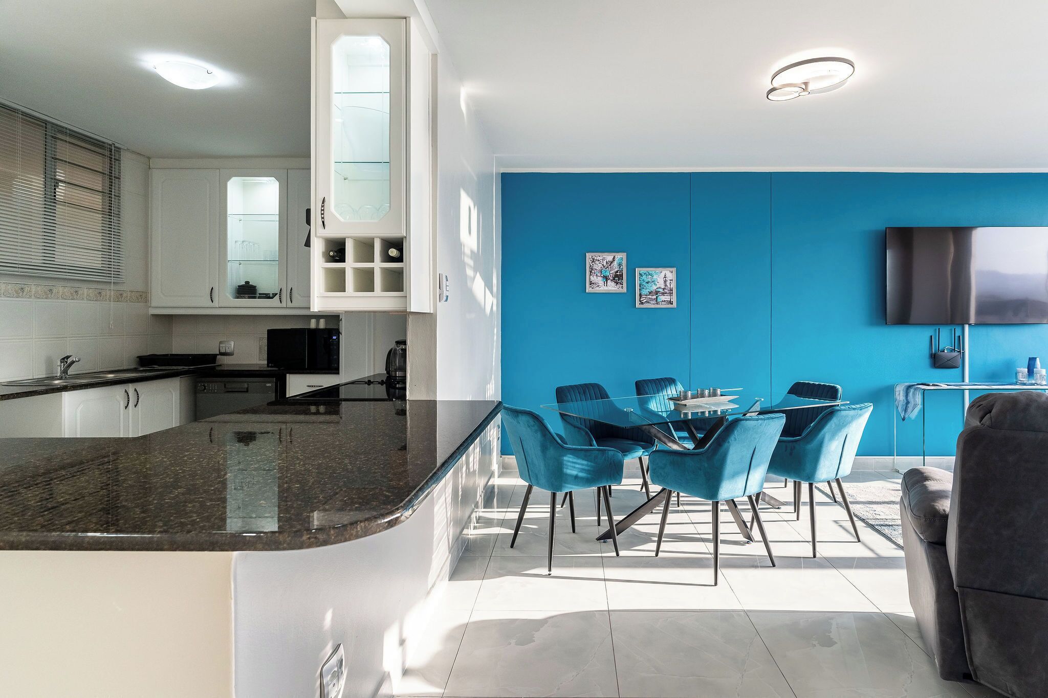 Una cocina moderna con armarios blancos, encimera de granito y un comedor con sillas azules.