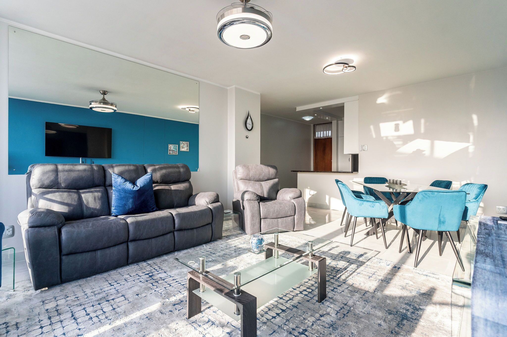 Een moderne woonkamer met een grijze bank, een glazen salontafel en blauwe stoelen.