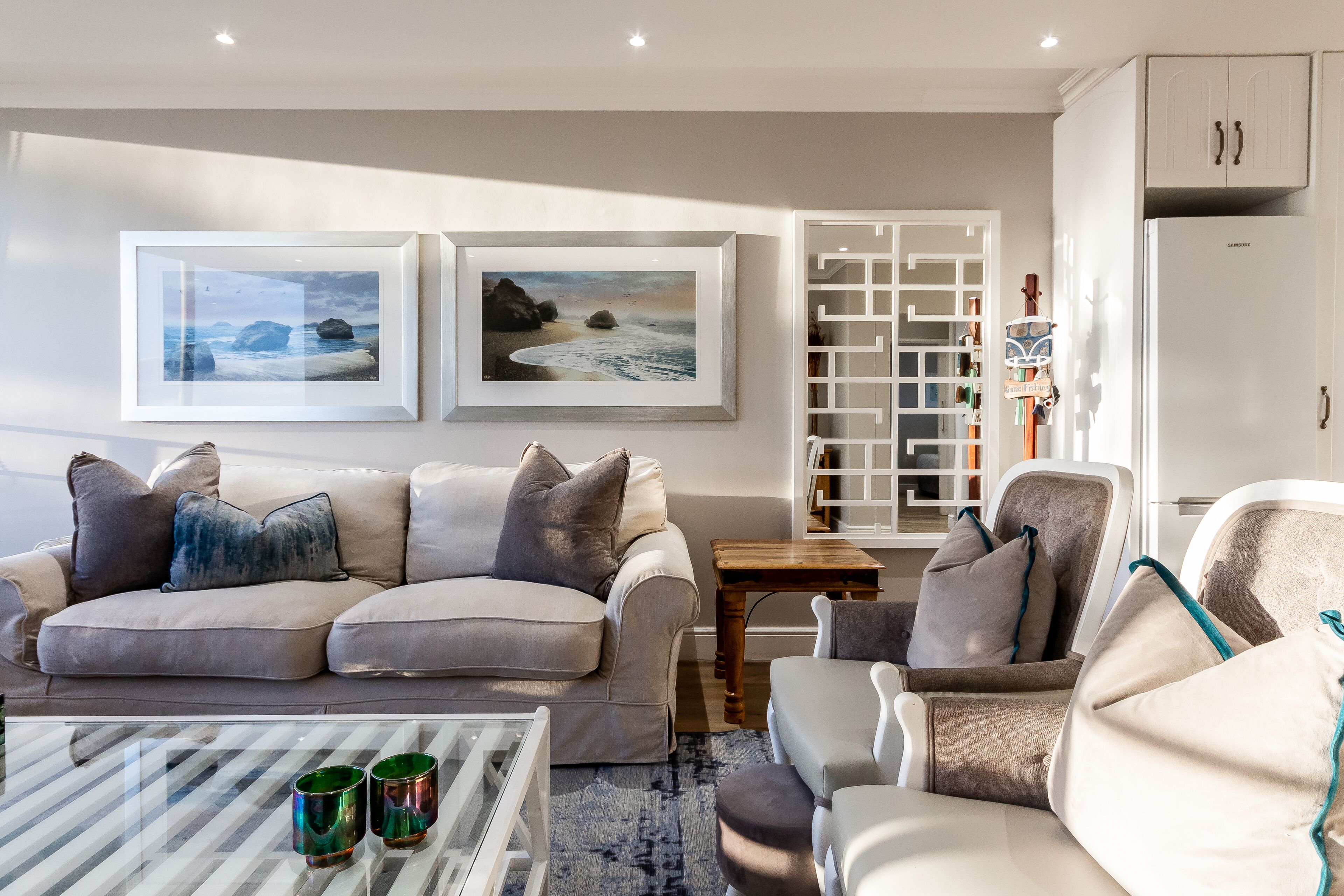 Una sala de estar moderna con un sofá color beige, una mesa de centro de vidrio y una estantería.