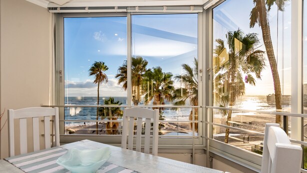 Ein Balkon mit Blick auf Strand und Meer, ausgestattet mit einem Tisch mit gestreifter Tischdecke und einer Glasbowl.