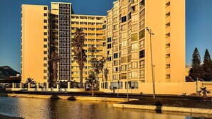 Ein Hochhaus mit mehreren Stockwerken, einem zentralen Innenhof mit Palmen und einem Gewässer im Vordergrund.