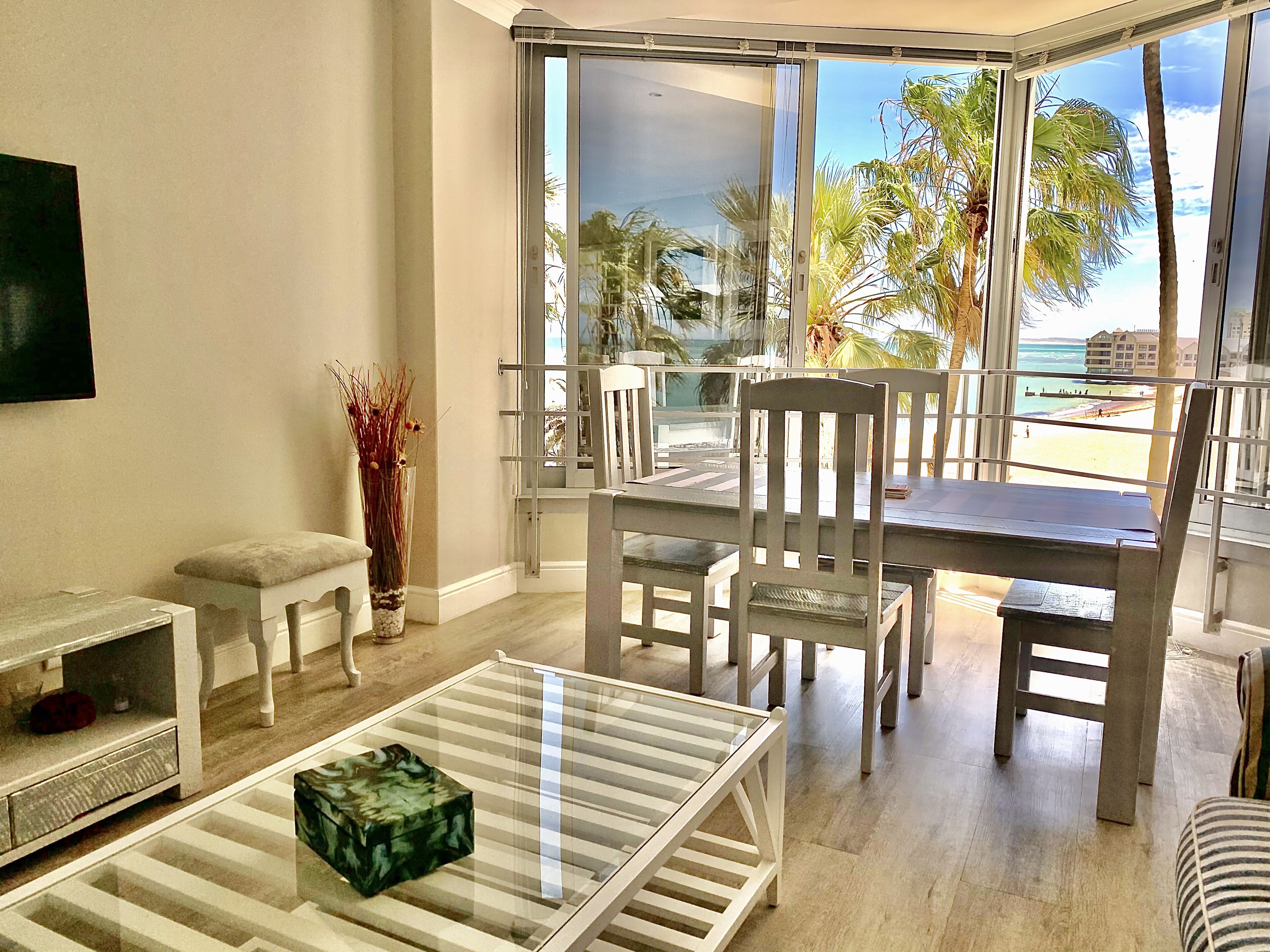A modern living room with a glass table, white chairs, a small side table, and a decorative vase.