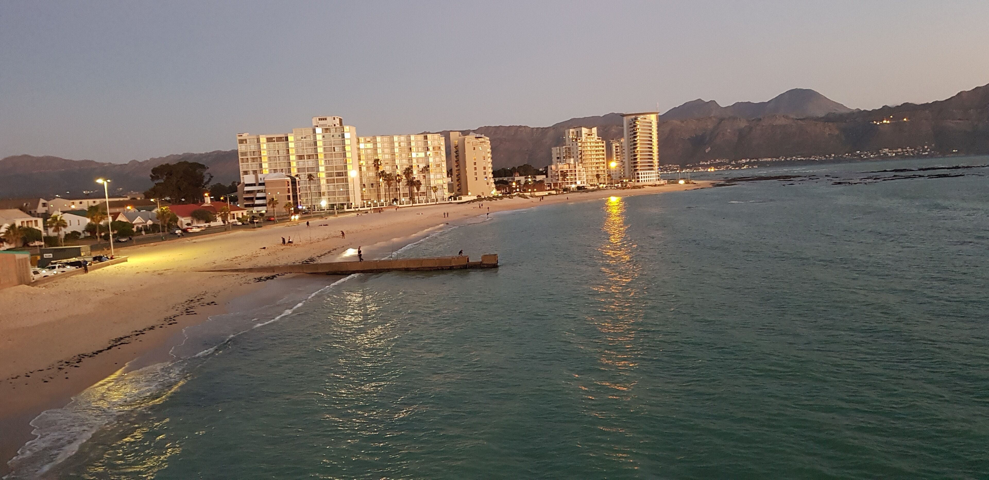 Een kuststreektzicht met een strand, gebouwen en bergen op de achtergrond.