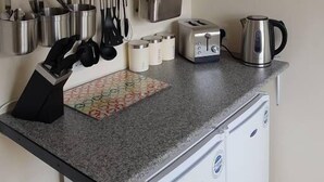 Uma cozinha compacta com armários brancos, torradeira, chaleira e diversos utensílios pendurados acima do balcão.