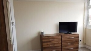 Quarto com cama, cómoda de madeira e televisão de tela plana, além de janela.