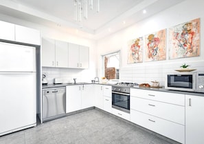 Une cuisine moderne avec des meubles blancs, des appareils en acier inoxydable et une Ćuvre dâart abstraite au mur.