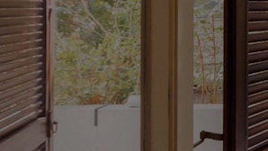 Ein Fenster mit Holzklappläden und Blick ins Grüne, an einer weißen Wand.
