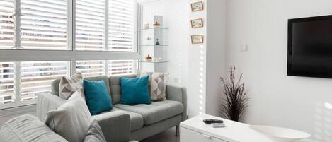A modern living room with a grey sofa, a white console table, and a large window with blinds.