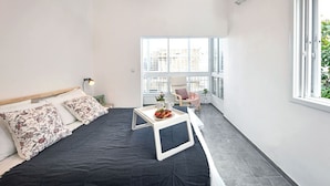 Ein modernes Schlafzimmer mit einem Bett, einem kleinen Tisch mit Obstplatte, einem Sessel und einem großen Fenster mit Stadtblick.
