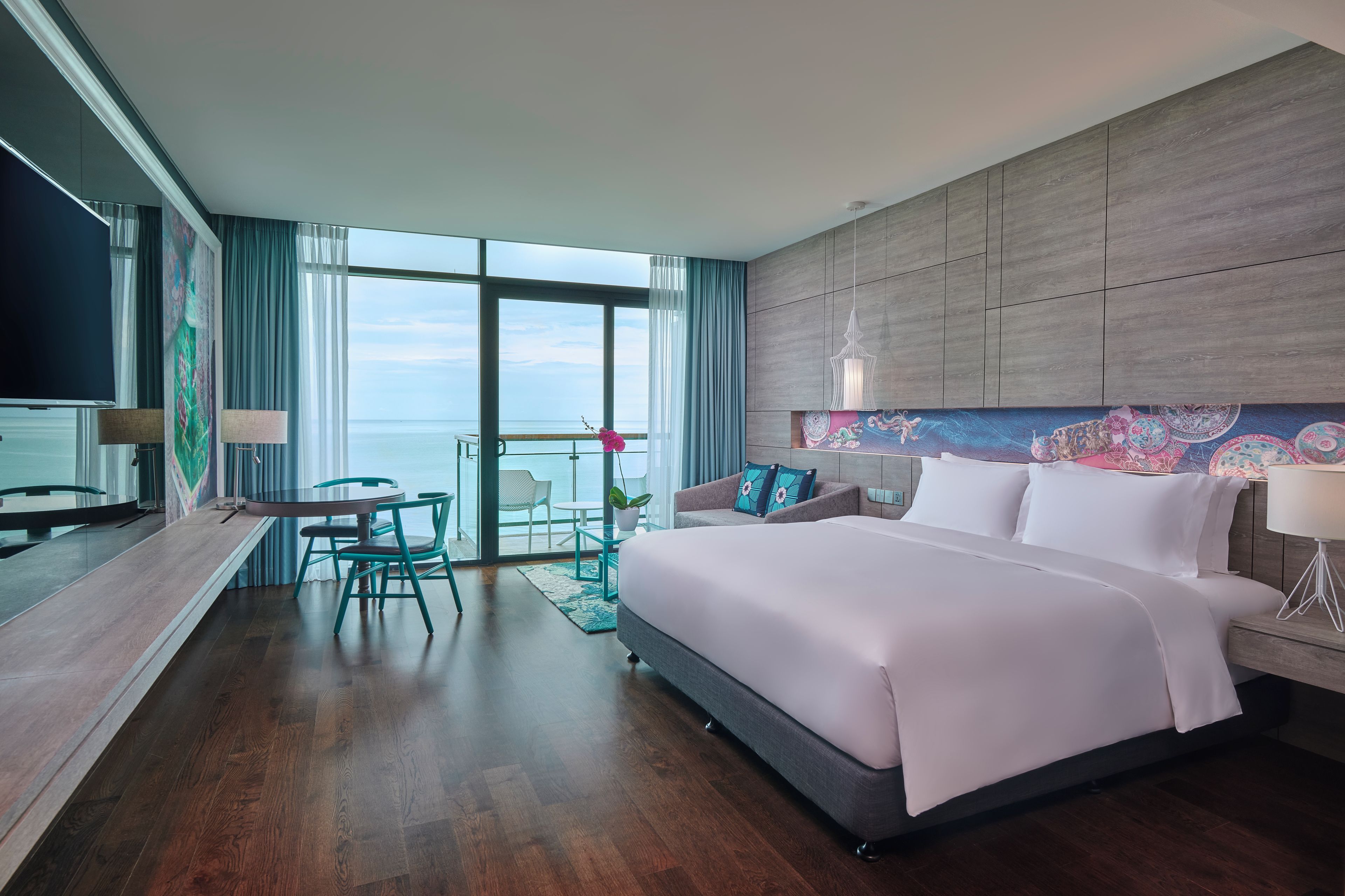Habitación de hotel con una cama grande, un escritorio con sillas, vista al mar y un balcón.