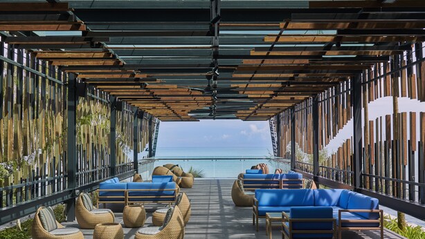 A covered outdoor seating area with wicker chairs and blue sofas, overlooking a body of water.