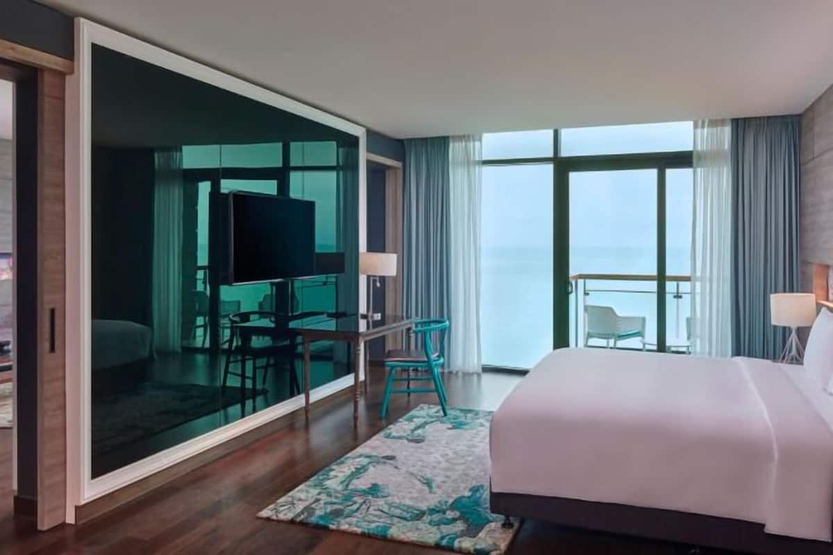 A hotel room with a bed, a TV, a balcony with a view, and a desk with a chair.
