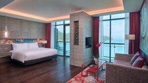A modern hotel room with a large bed, a sofa, a TV, and a balcony with a view of the sea.
