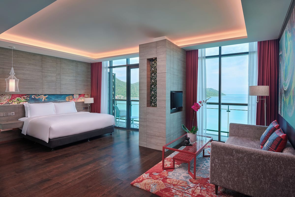 A modern hotel room with a large bed, a sofa, a TV, and a balcony with a view of the sea.