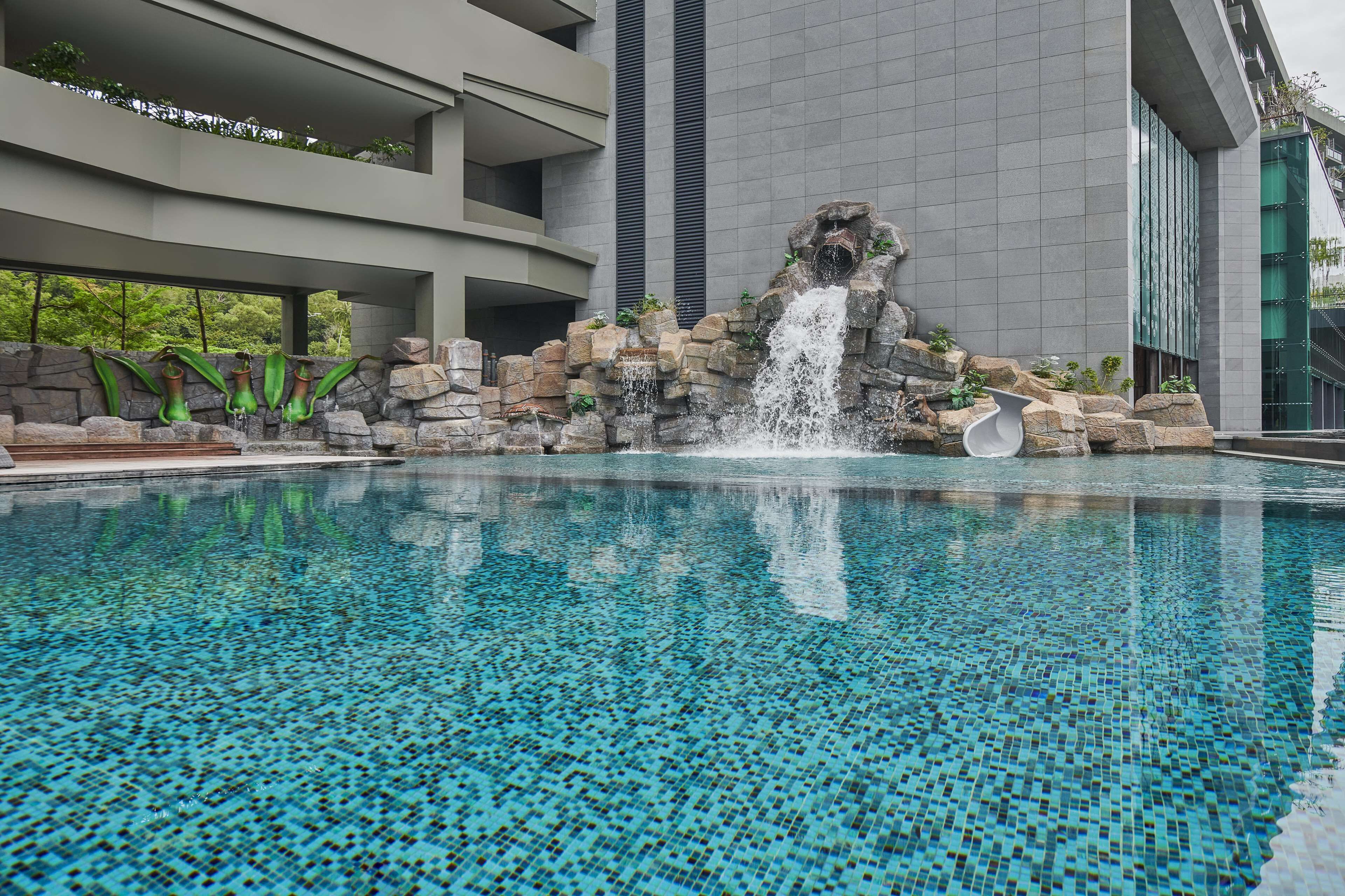 Une piscine agrémentée d’une cascade, entourée d’un mur de pierre et de verdure.