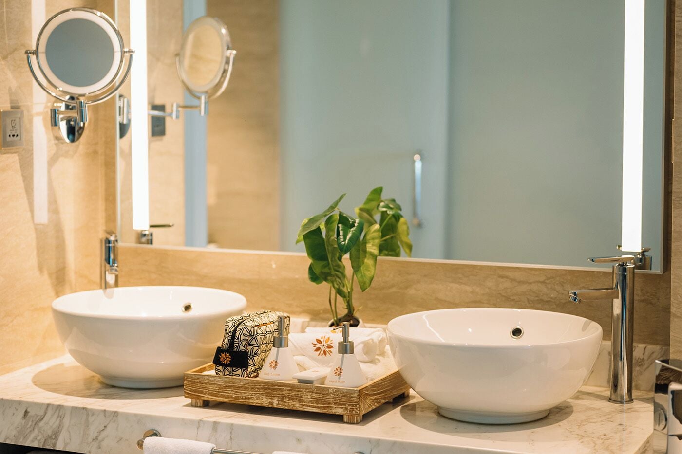 A bathroom with two white vessel sinks, a mirror, and a small plant on a wooden tray.