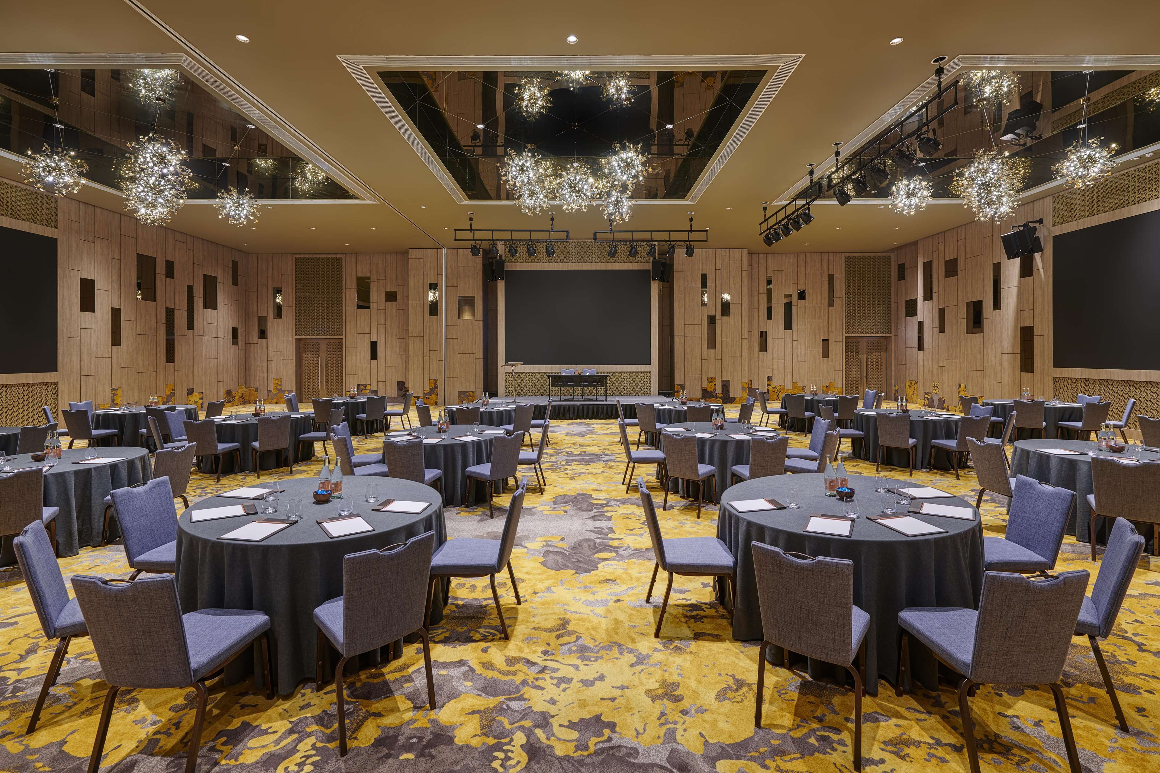 A conference room with round tables, chairs, a stage, and a carpeted floor.
