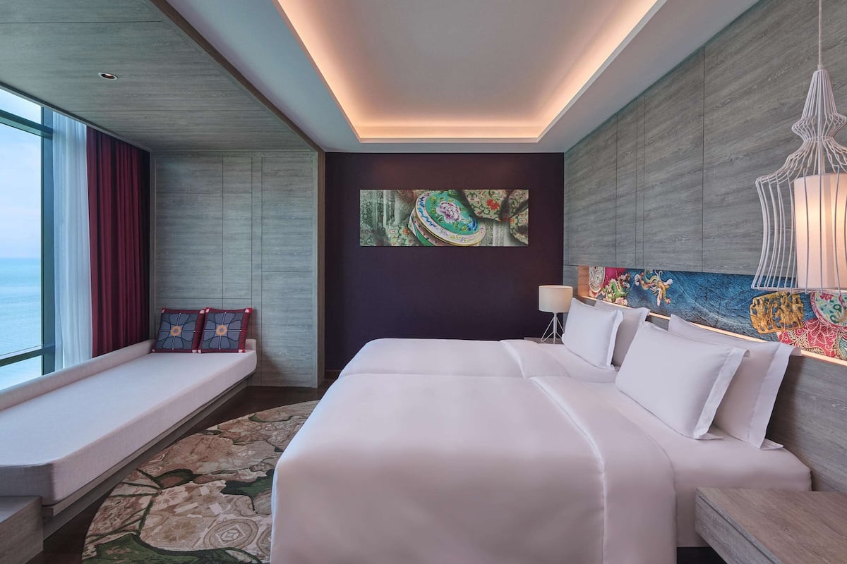 A modern hotel room with a large bed, a seating area by the window, and artwork on the walls.