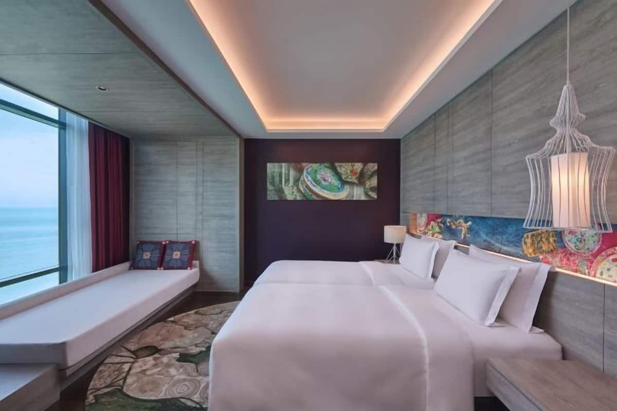 A modern hotel room with a large bed, a seating area by the window, and a view of the ocean.