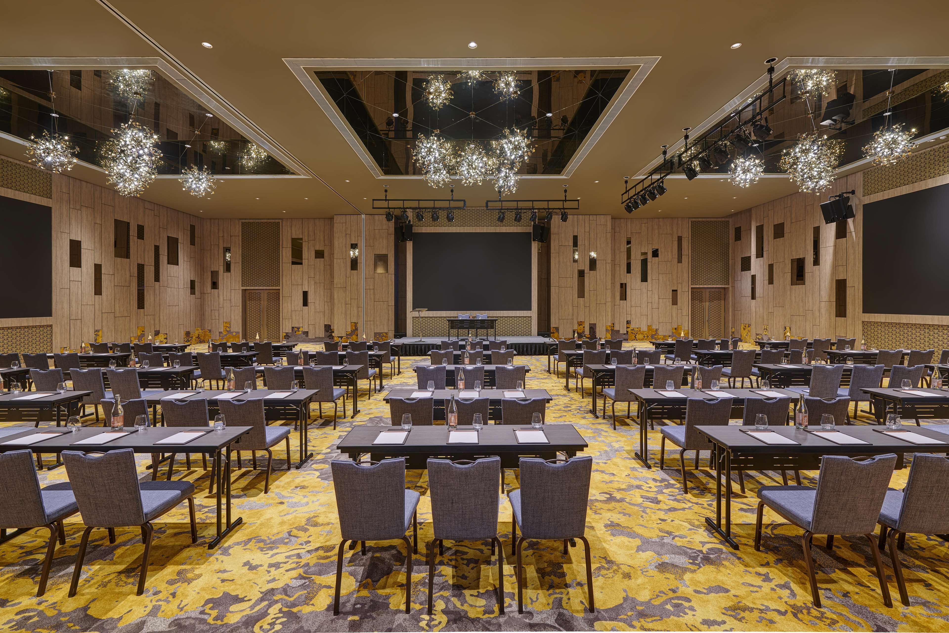 A conference room with multiple tables and chairs, a large screen, and a patterned carpet.