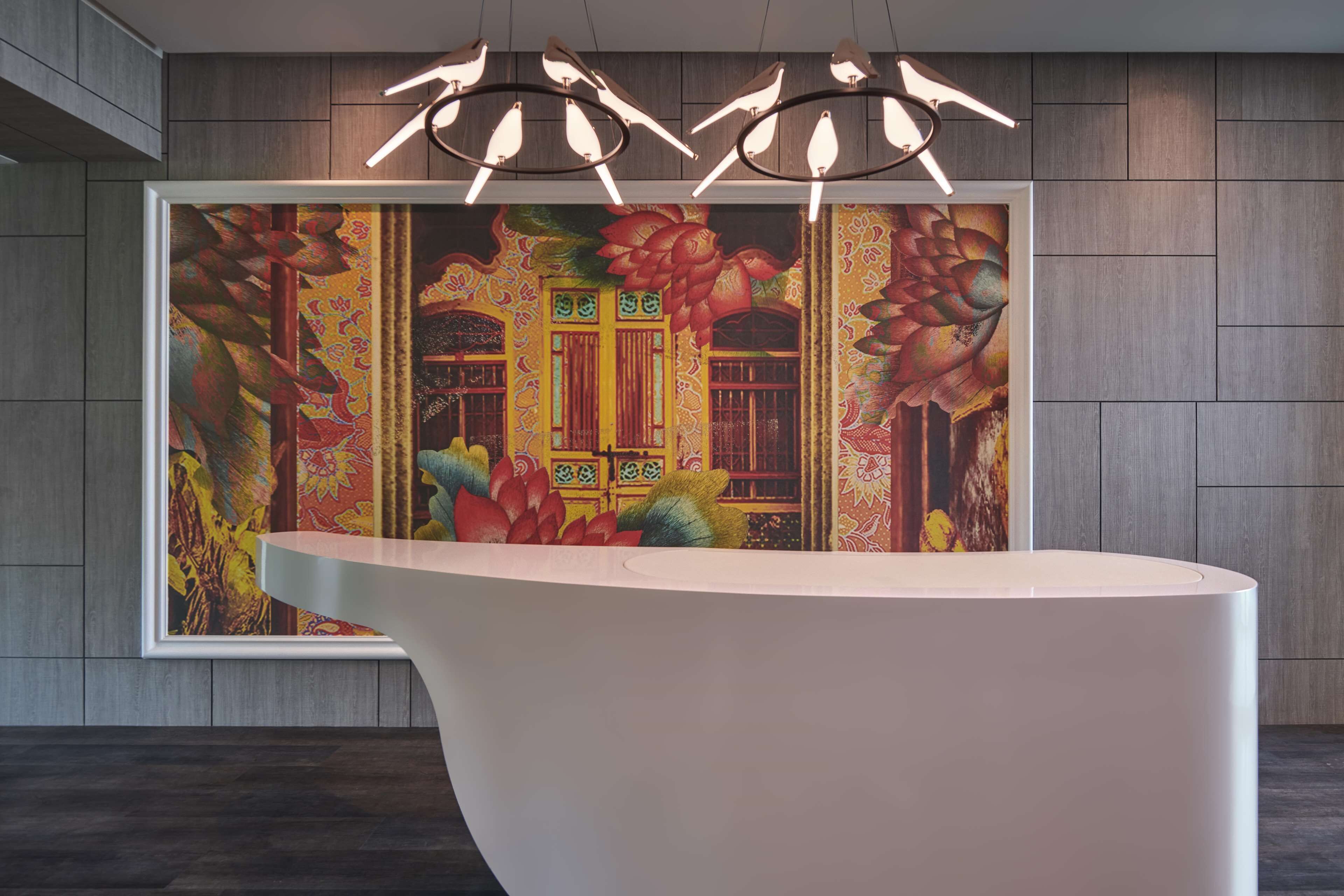 A reception desk with a modern design, a colorful mural with traditional architecture, and a unique bird-shaped light fixture above.