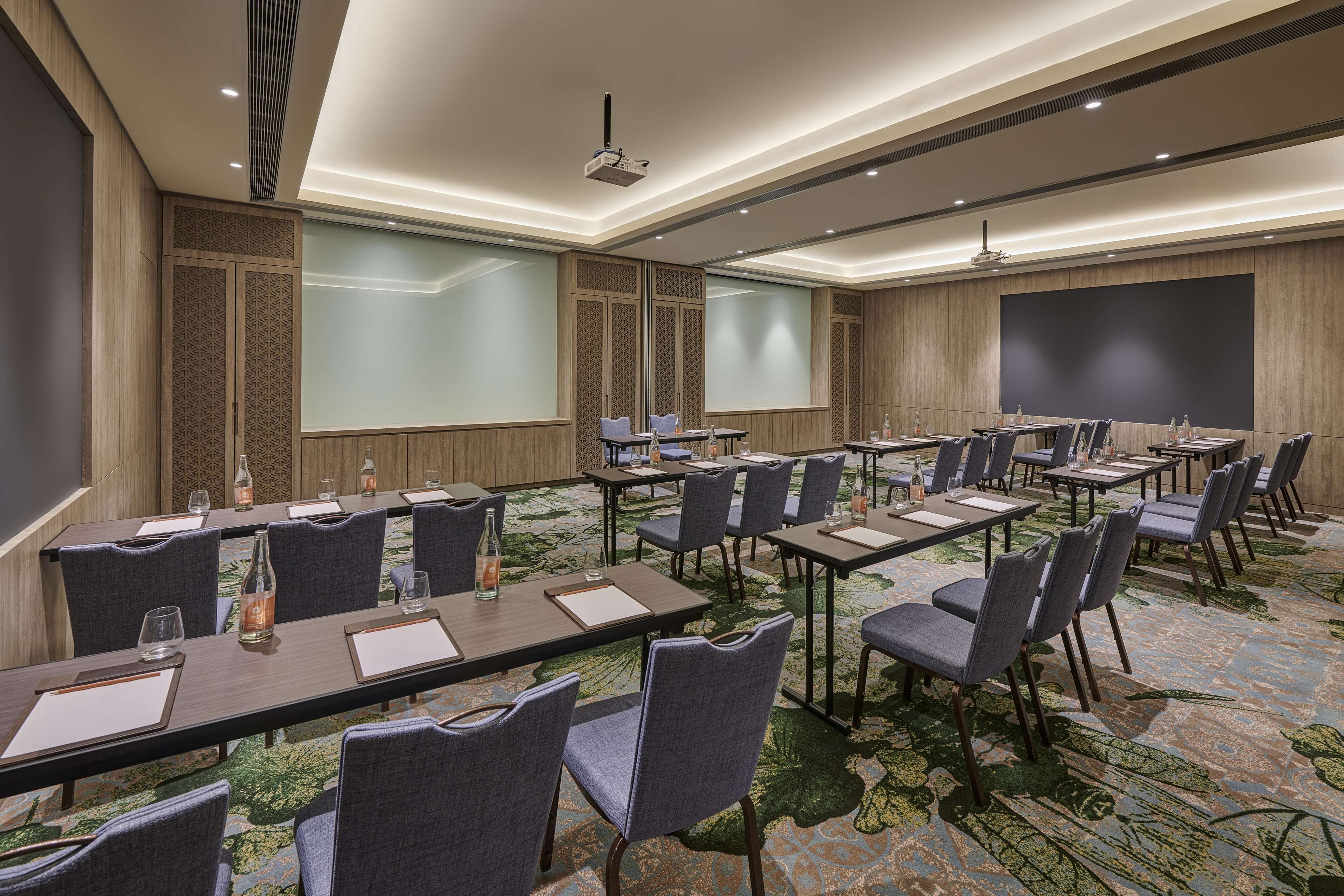 A conference room with multiple tables, chairs, and a large screen.