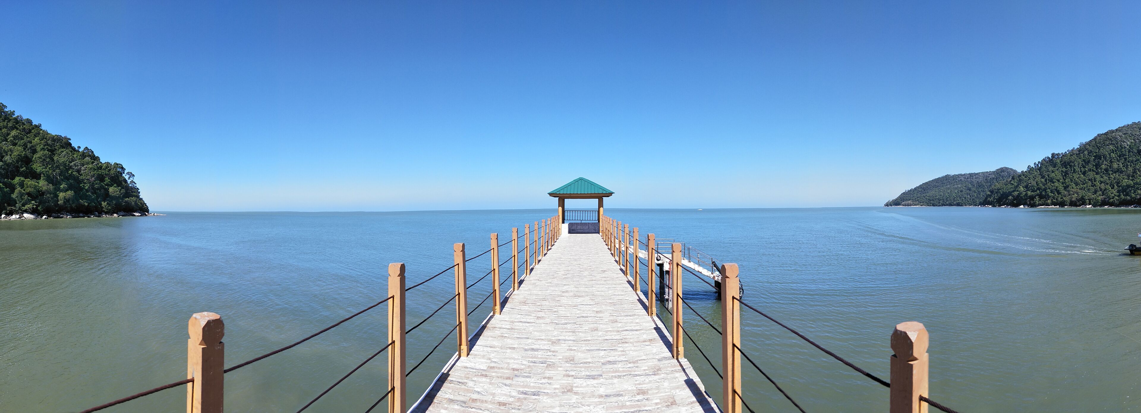 A wooden pier leading to a gazebo over water, surrounded by hills.