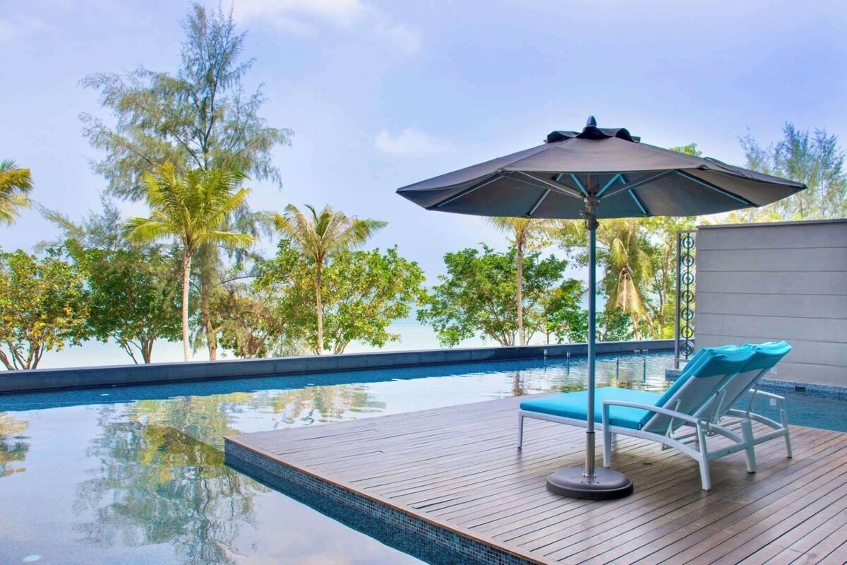 A pool area with a wooden deck, lounge chairs, and an umbrella.