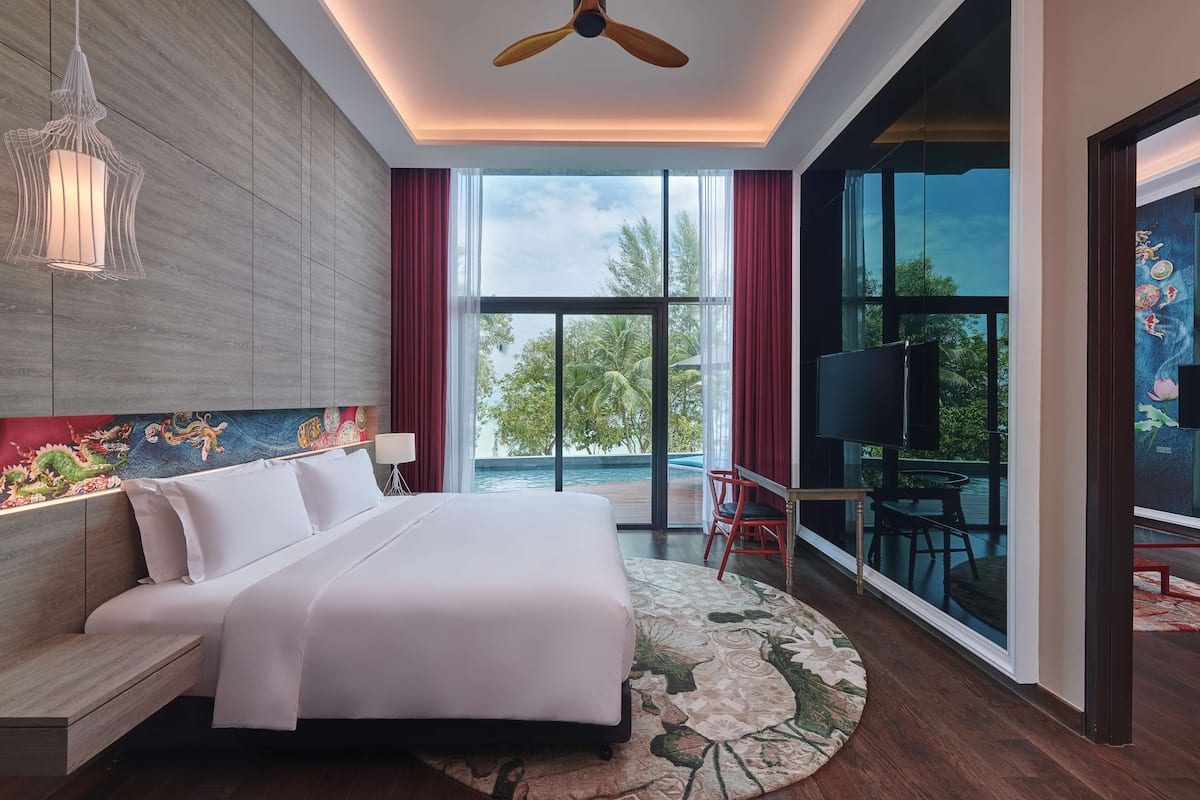 A modern hotel room with a large bed, a ceiling fan, a TV, and a balcony with a view of the outdoors.