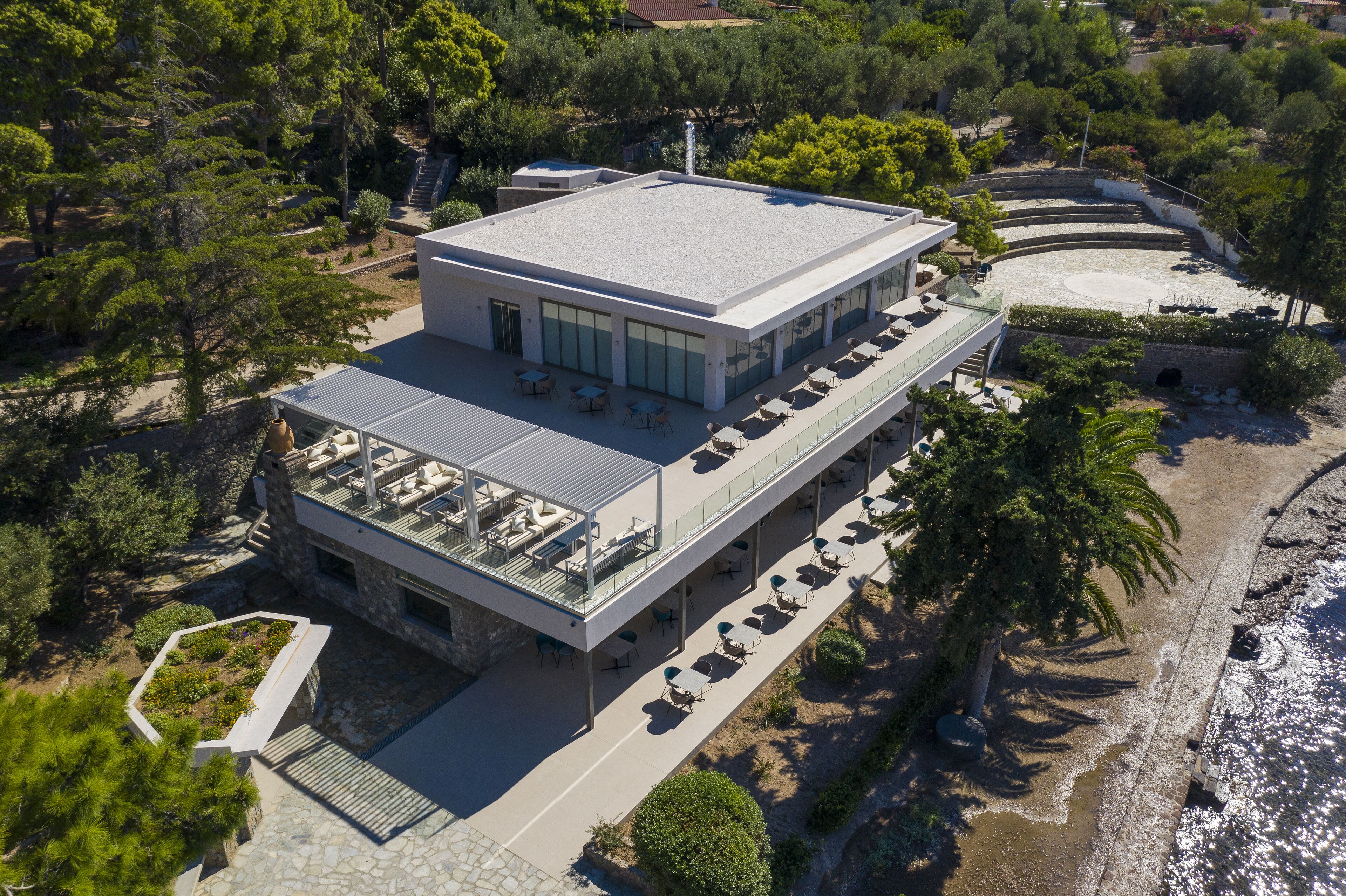 An aerial view of a modern hotel with a flat roof, outdoor seating area, and a pool.