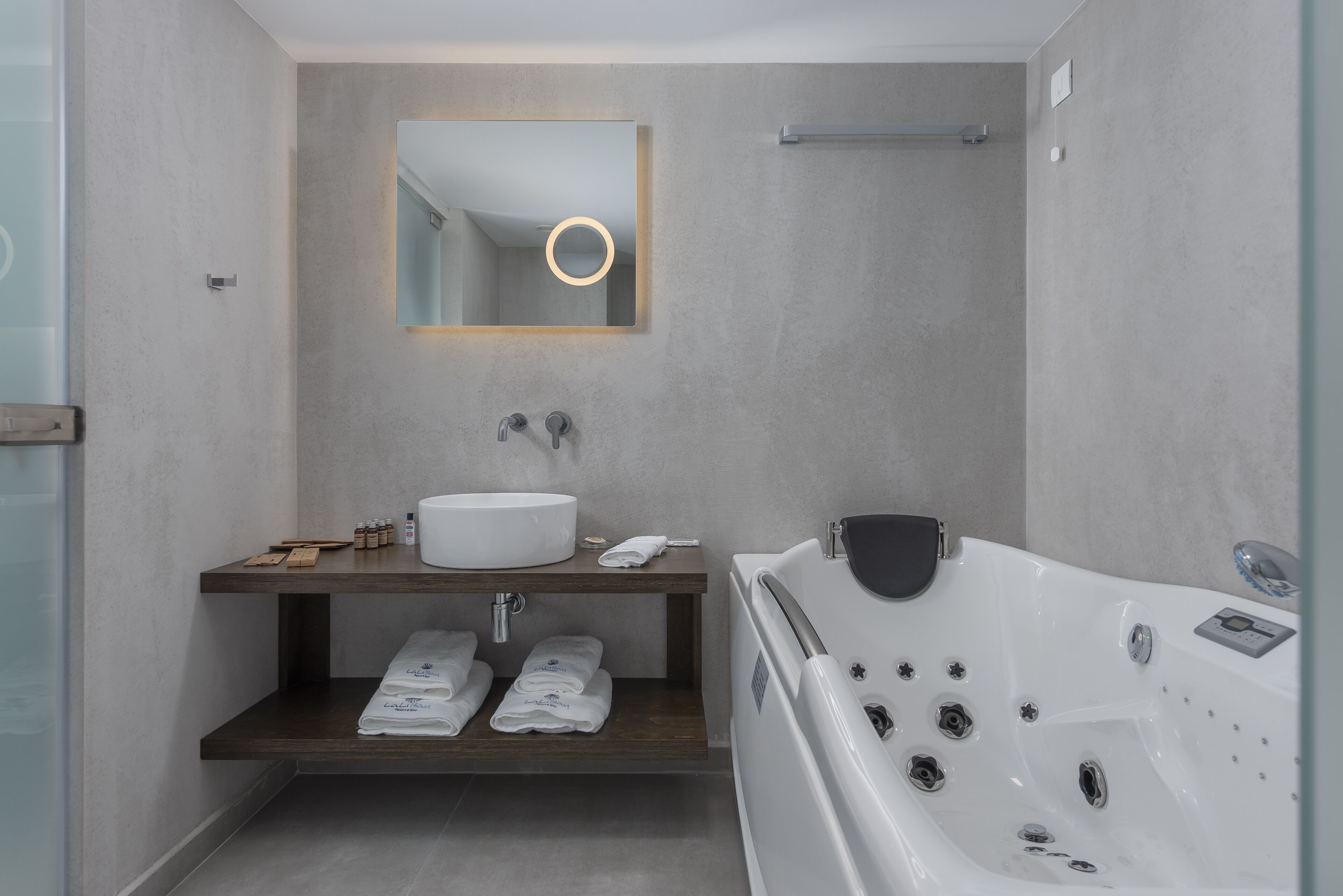 A modern bathroom with a large bathtub, a round mirror, and a wooden vanity with towels.