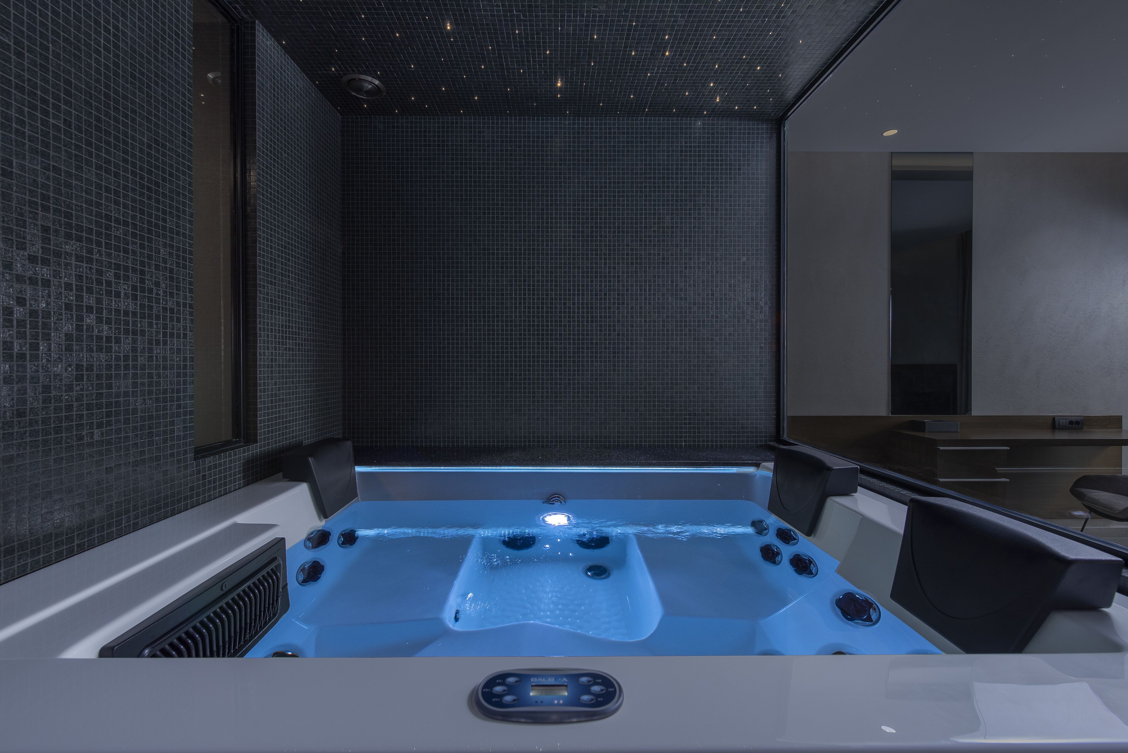 A modern spa room with a large bathtub, a control panel, and a tiled wall.