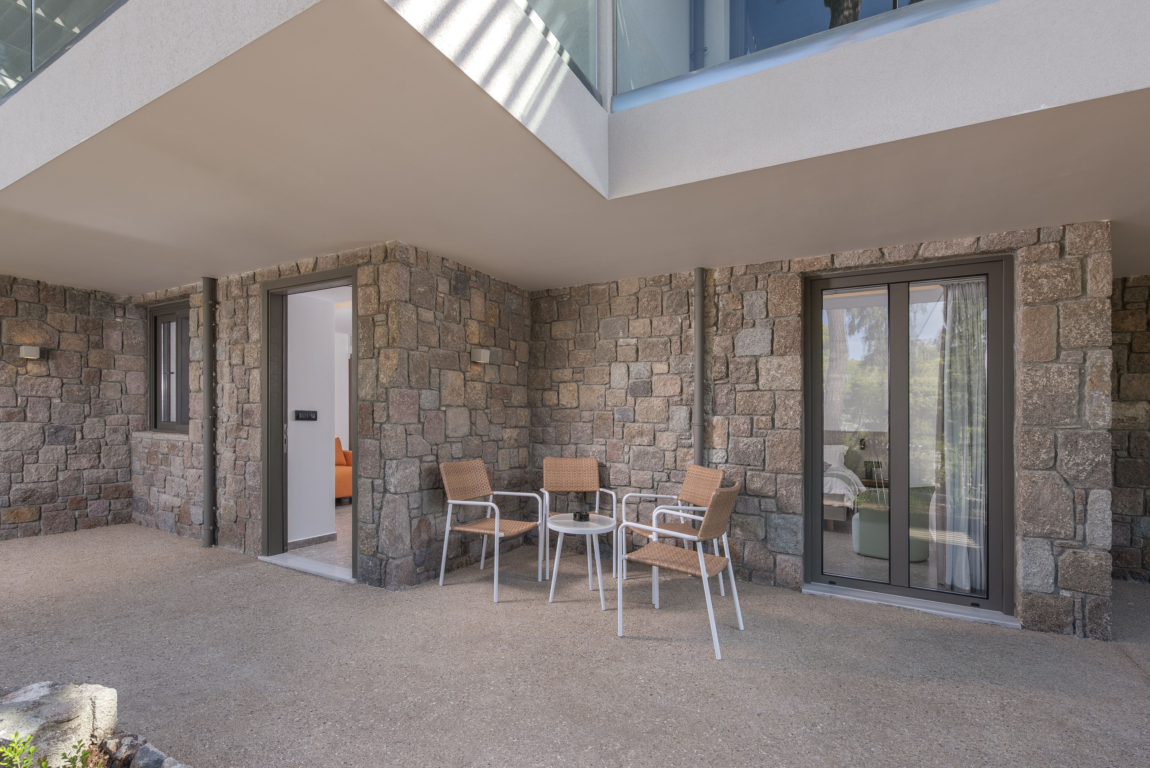 Eine moderne Außenpatio mit Steinmauern, einer Glastür und einer Sitzecke mit Stühlen und einem Tisch.