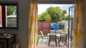 Ein Zimmer mit einer Schiebetür, die auf eine Außenpatio führt. Auf der Terrasse stehen ein Tisch und Stühle, und draußen ist ein blaues Fahrzeug geparkt.