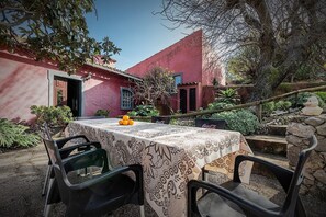A patio with a table set for two, surrounded by chairs, with a red building in the background.
