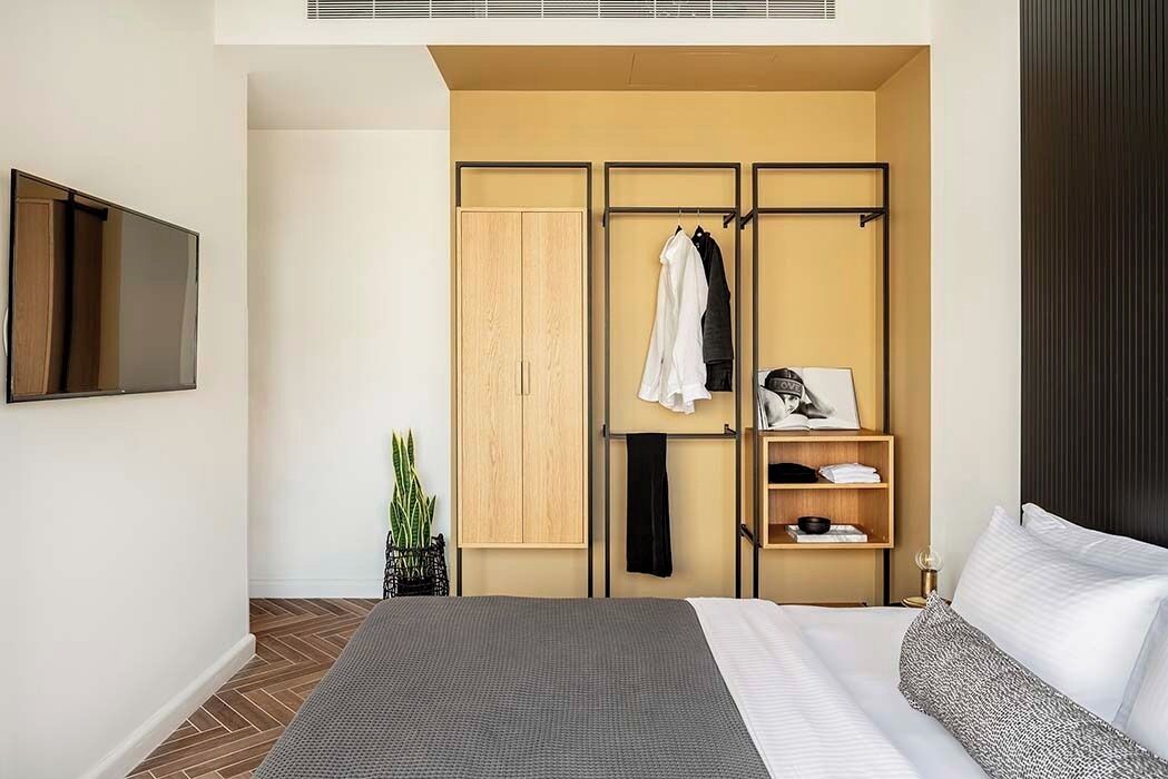 Une chambre d’hôtel moderne équipée d’un lit, d’une armoire, d’une étagère avec des vêtements pliés, d’une petite plante et d’un téléviseur à écran plat.