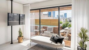 A modern living room with a large TV, a sofa, and a balcony with outdoor seating. - Mr. Louis - By TLV2GO (Tel Aviv)