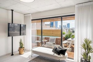 Ein modernes Wohnzimmer mit großem Fernseher, einer Couch und einem Balkon mit Sitzgelegenheit.