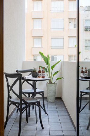A small balcony with a table, chairs, a potted plant, and bottles.